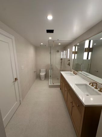 Modern bathroom with double vanity, large mirror, glass shower, and toilet on light tile floor