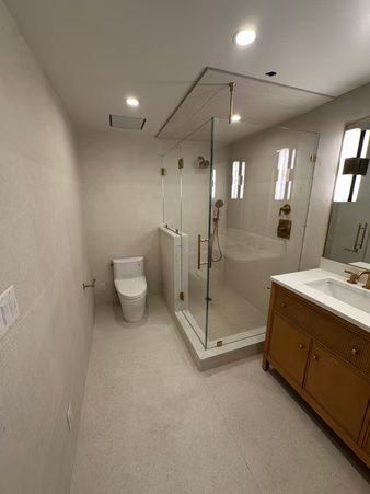 Modern bathroom with glass shower, toilet, and wooden vanity in a bright, tiled space