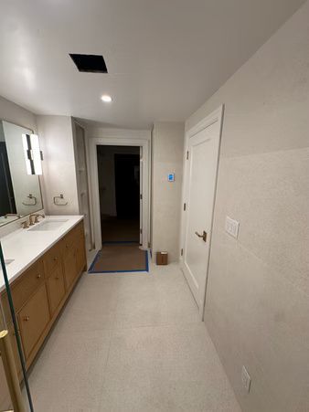 Narrow hallway with bathroom vanity on the left, white walls, and an open doorway at the end.