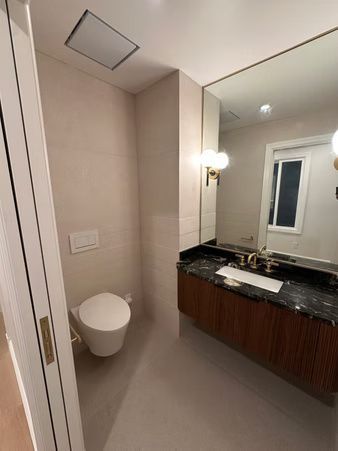 Small bathroom with wall-mounted toilet, vanity, large mirror, and beige walls.