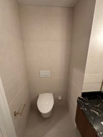 Small narrow bathroom with a wall-mounted toilet and beige tiled walls
