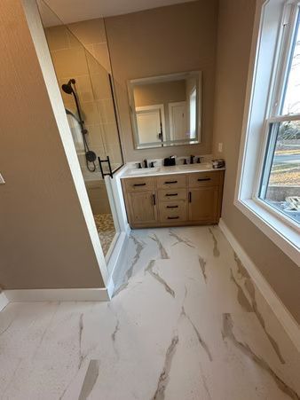 Modern bathroom with tan walls, white veined floor tile, double vanity, mirror, and large window