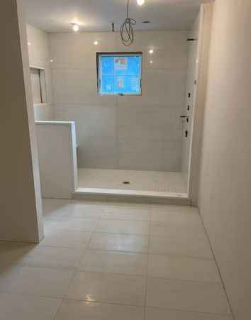 Empty tiled bathroom with a walk-in shower and small window above the shower stall