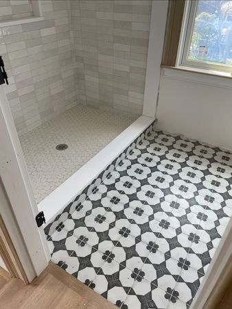 Bathroom with tiled shower, patterned black-and-white floor, and window light