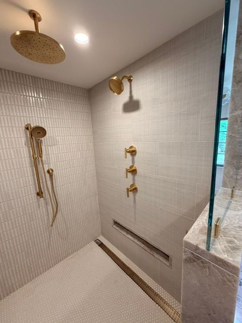 Modern shower with gold fixtures, tiled walls, bench, and marble accent ledge.