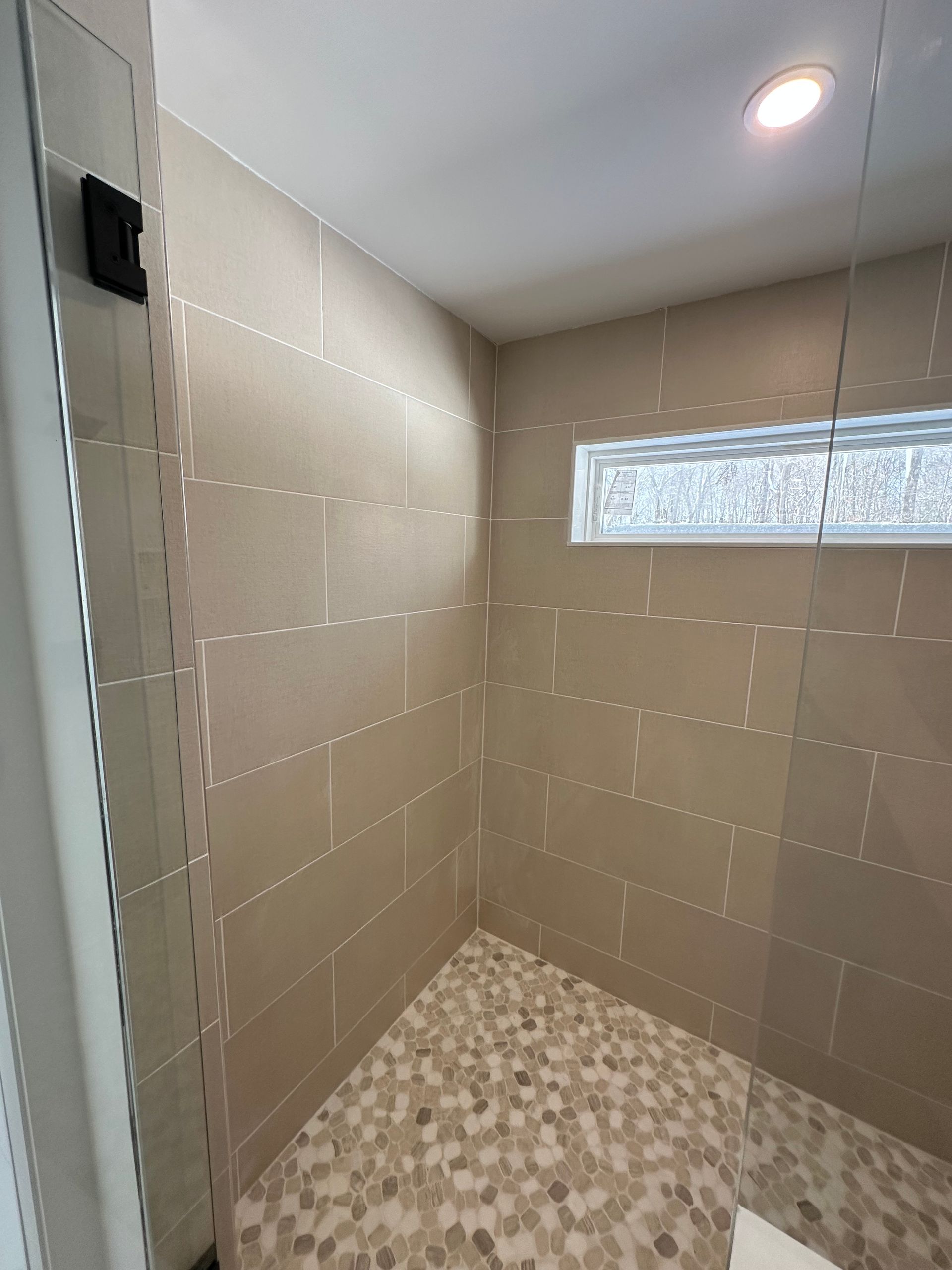 Empty tiled shower with beige walls, mosaic floor, recessed light, and frosted window.
