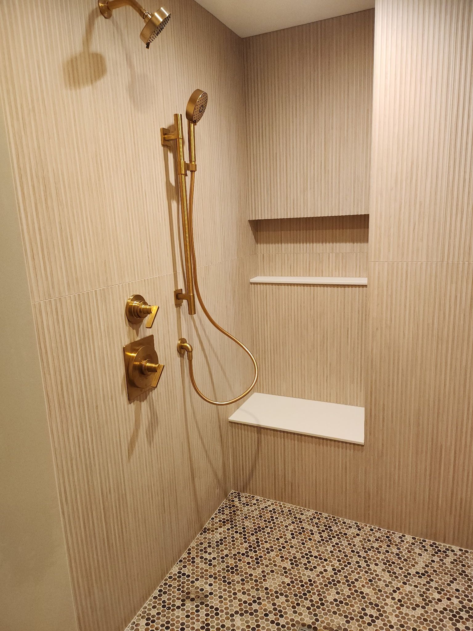 Gold shower fixtures in a small tiled walk-in shower with built-in shelves and patterned floor.