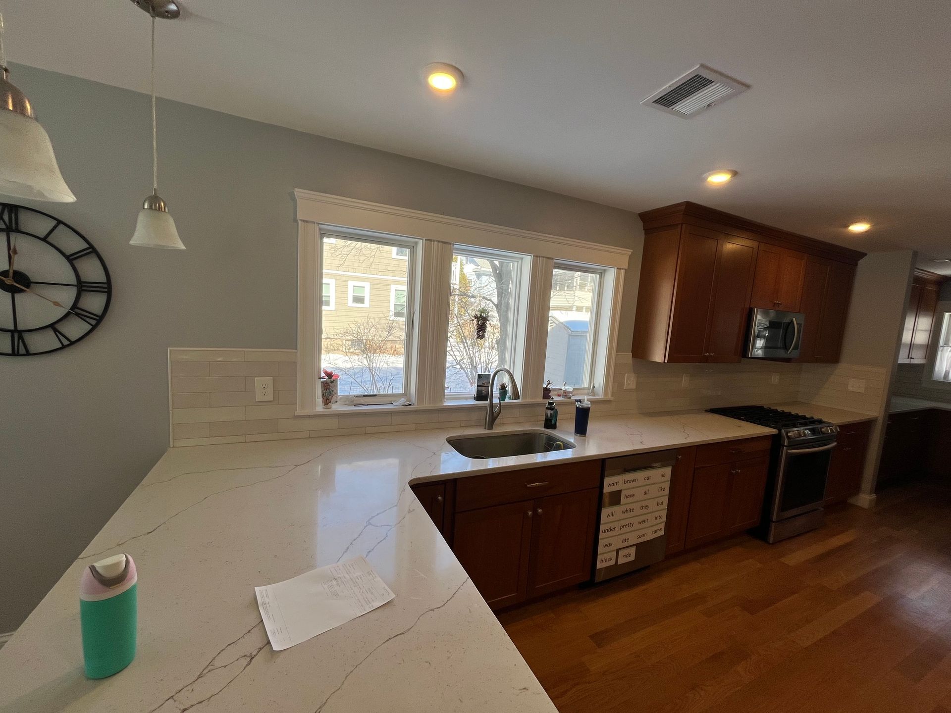 Modern kitchen with white counters, wood cabinets, sink by window, and a teal tumbler on the island.
