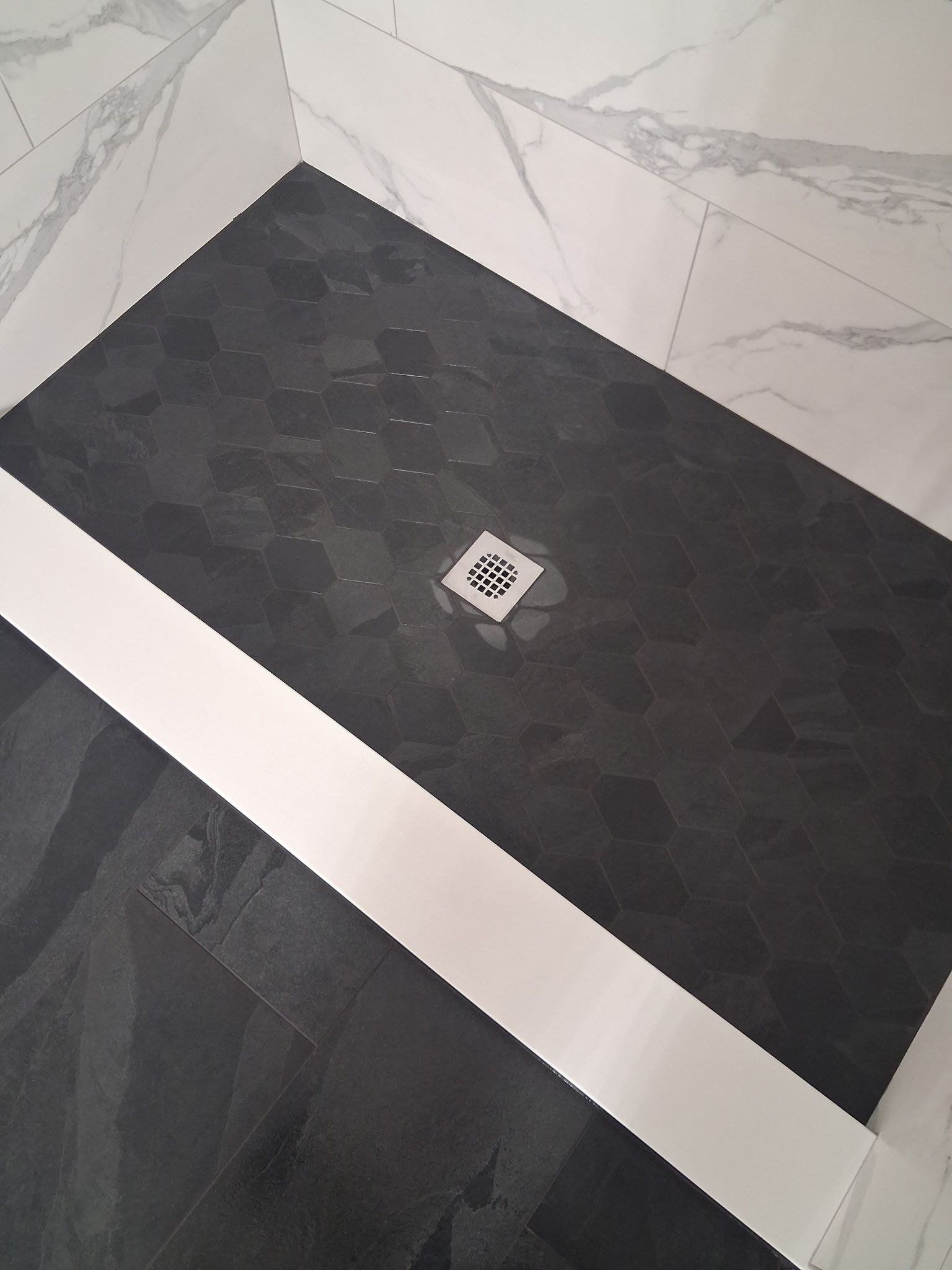 Black tiled corner with a small square drain cover on the floor.