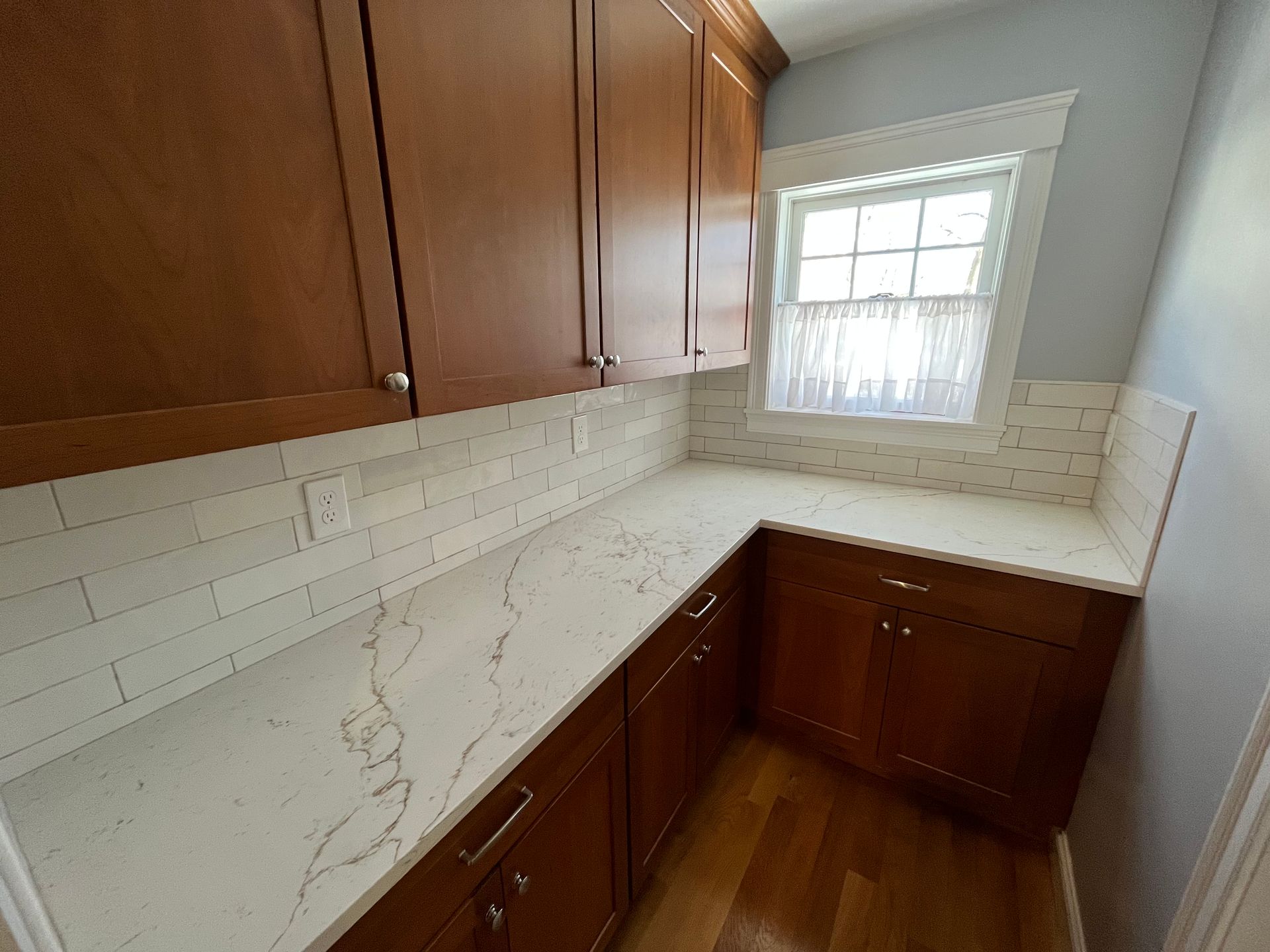 Compact kitchen with wood cabinets, white marble-look counters, and a small window above the sink.