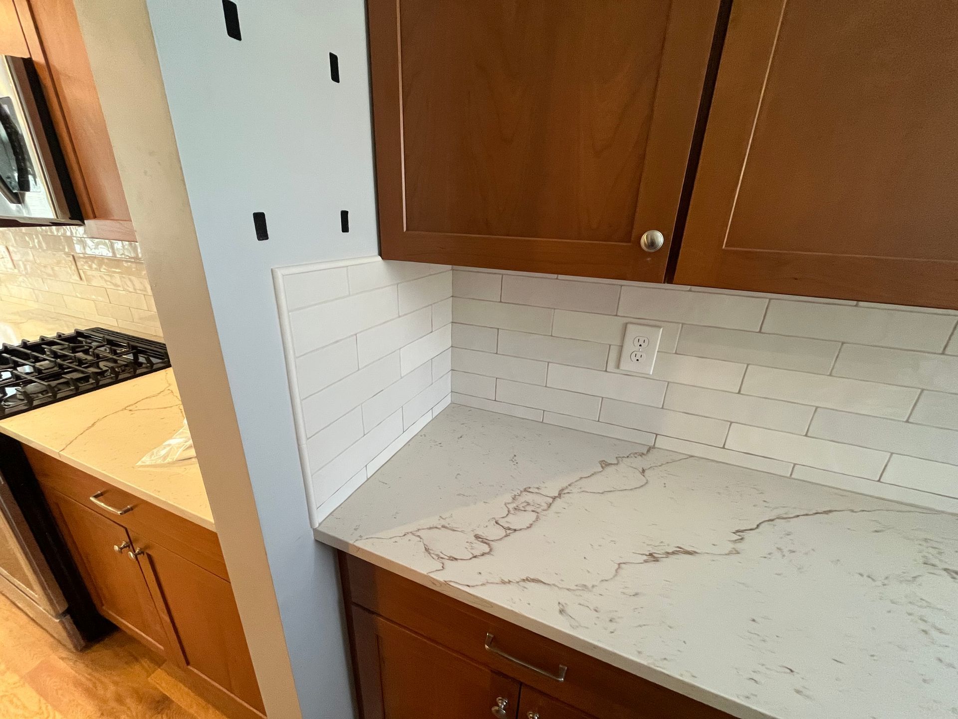 Small kitchen corner with white subway tile backsplash, wood cabinets, and a light stone countertop.