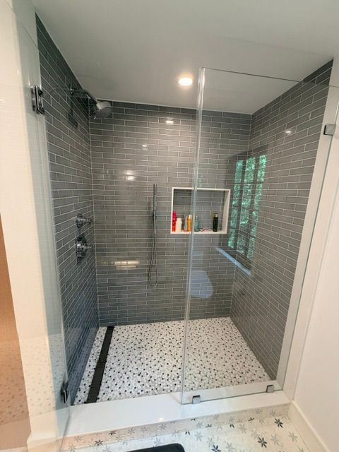 Modern walk-in shower with gray tile, white pebble floor, glass enclosure, and built-in shelf.