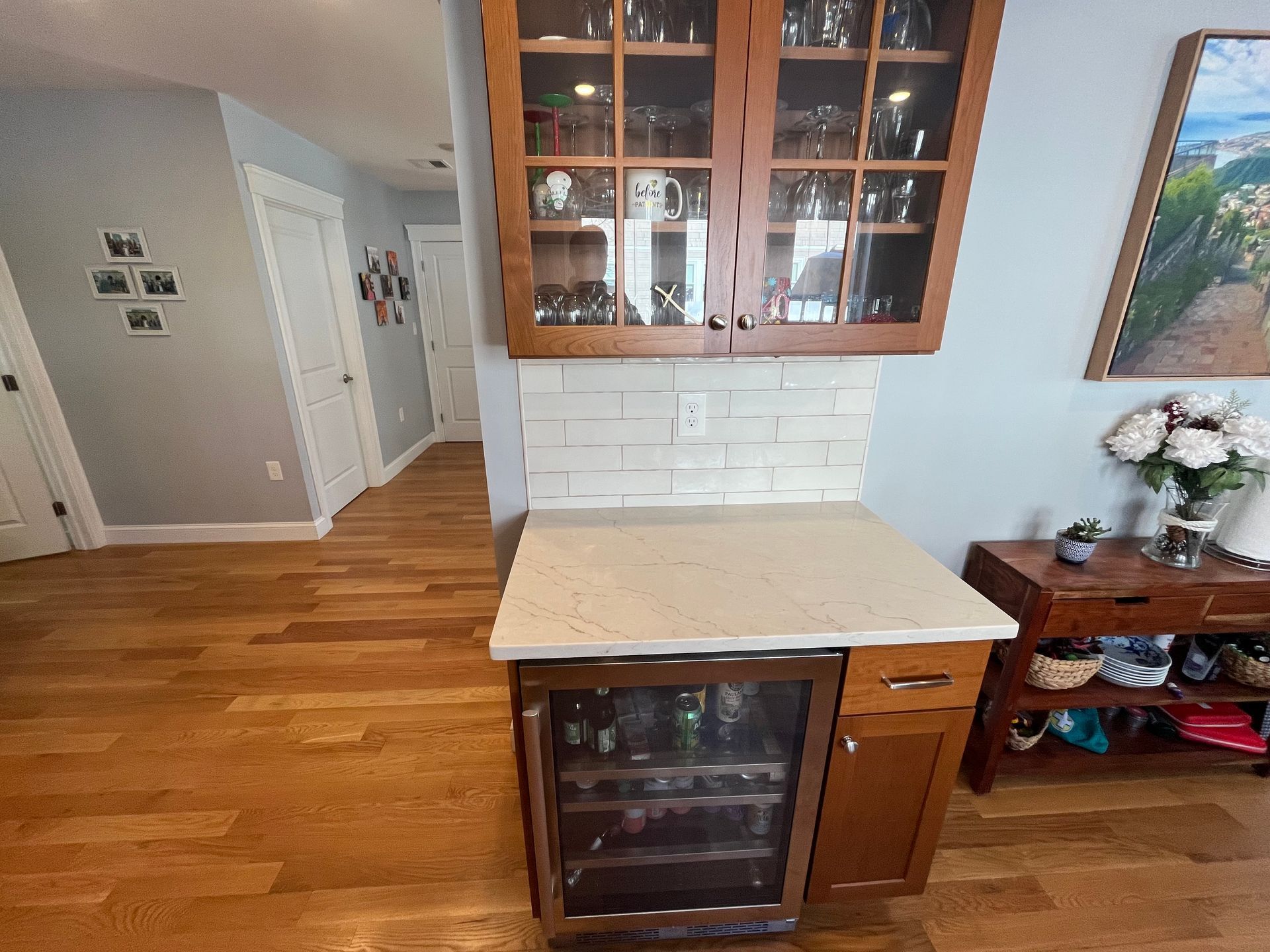 Kitchen nook with white countertop, glass-front cabinet, and hardwood floors in a bright home interior