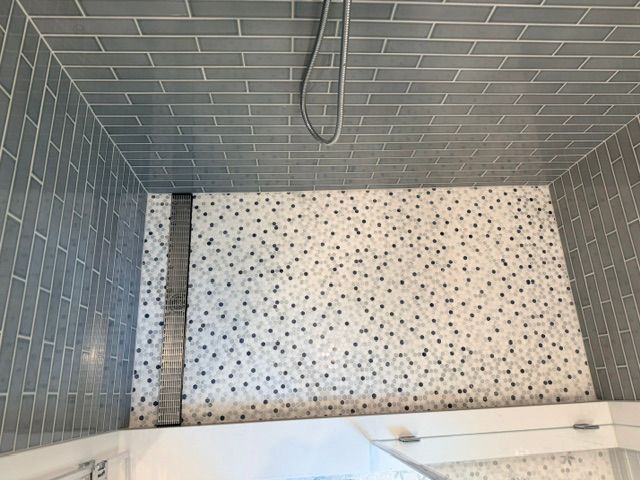 Empty tiled shower with gray walls and a white speckled floor, viewed from above.