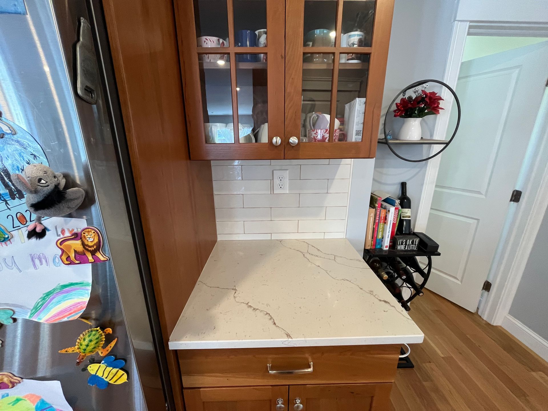 Kitchen nook with beige countertop, wood cabinets, and a small side table with books and decor.