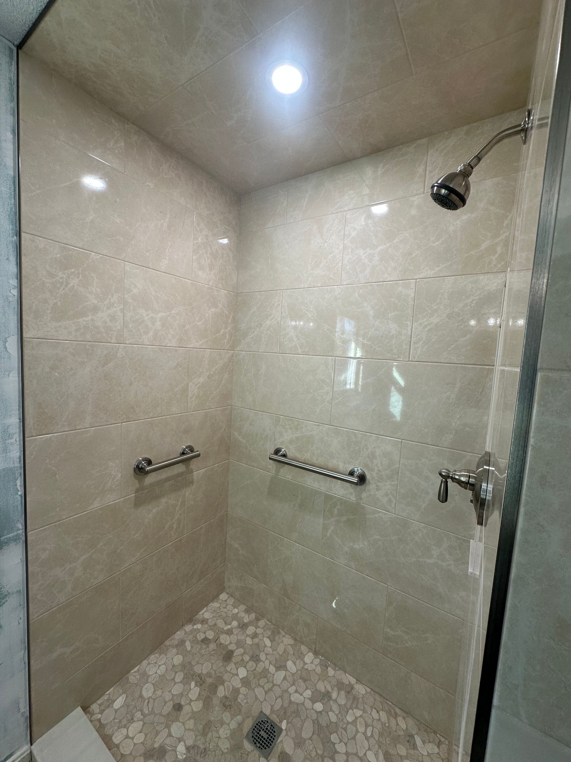 Empty tiled shower stall with built-in grab bars and a showerhead under a ceiling light