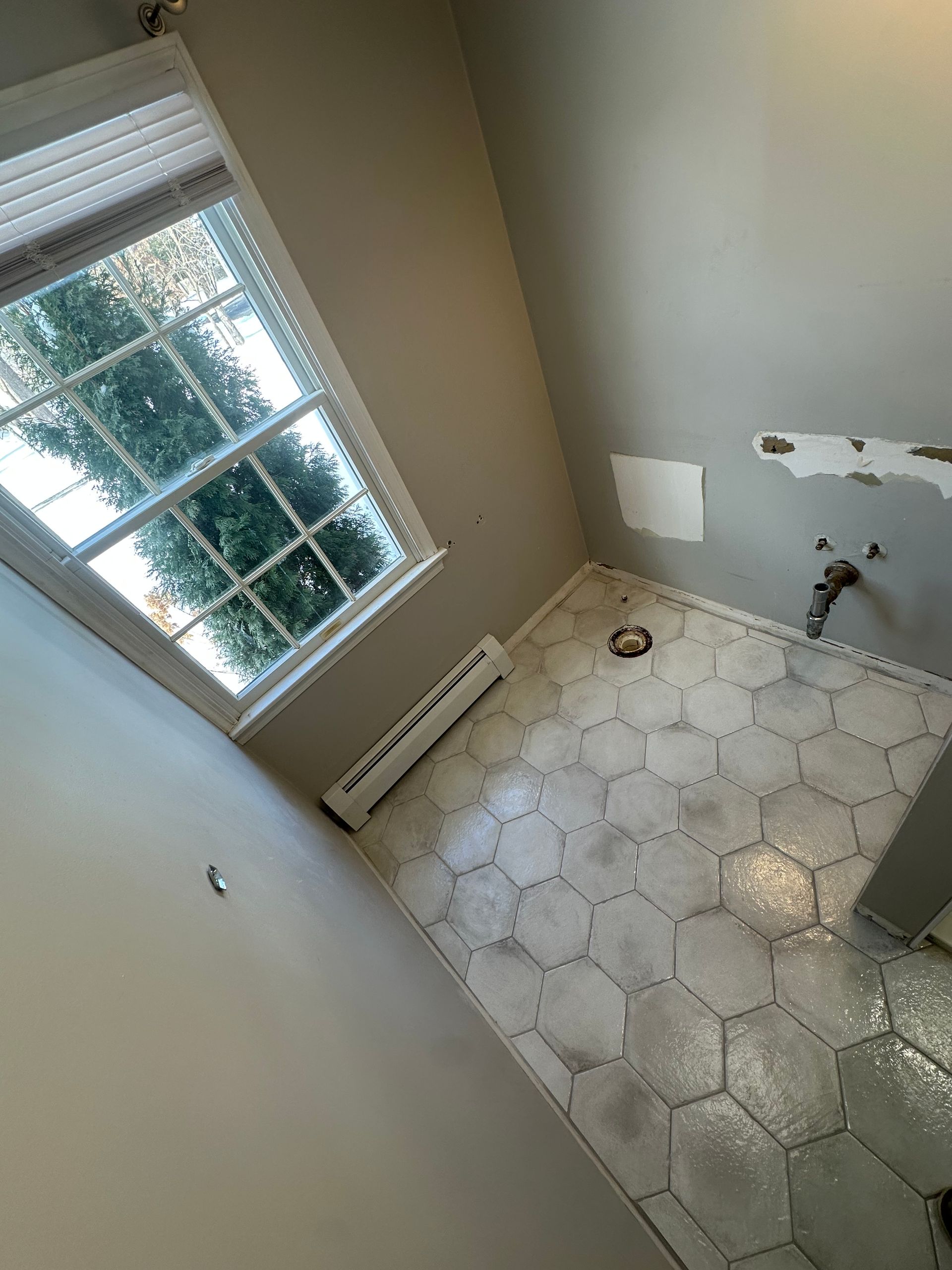 Empty tiled bathroom with a window, toilet area, and light-colored walls.