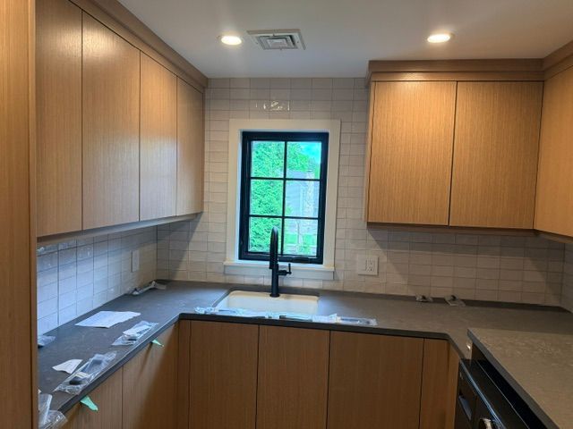 Modern kitchen with wood cabinets, white tile backsplash, black faucet, and a window above the sink.