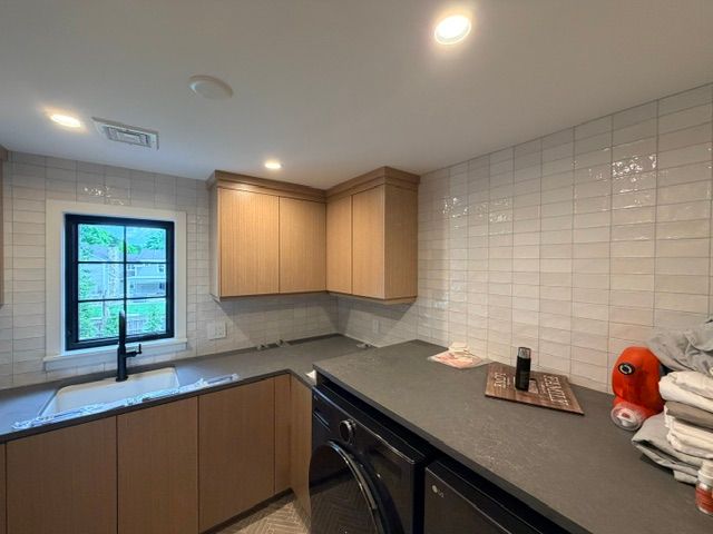 Modern kitchen with wood cabinets, gray counters, tile backsplash, and a window above the sink.
