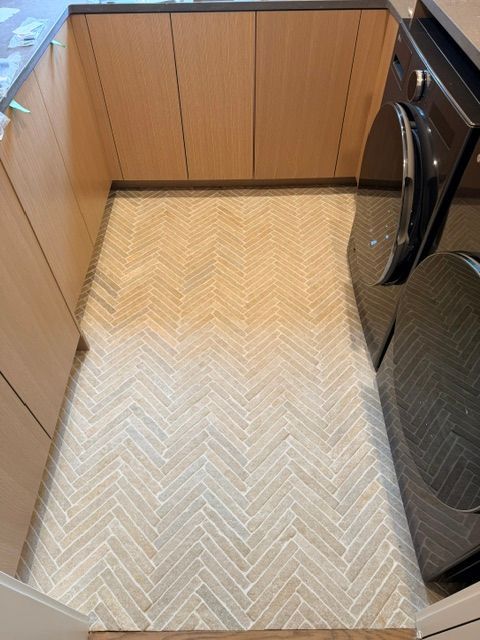 Narrow kitchen floor with light herringbone rug between wood cabinets and appliances.