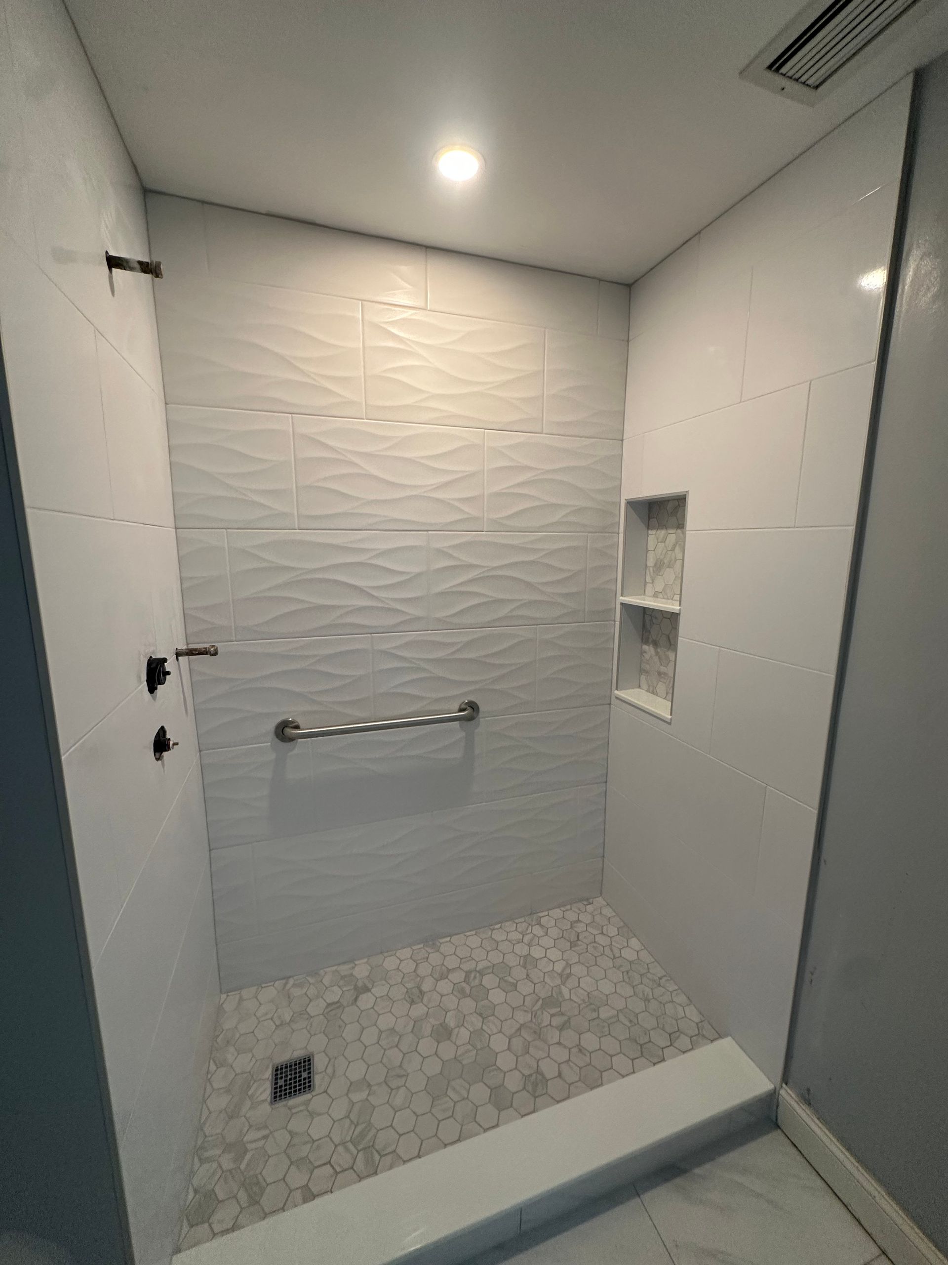 Empty modern shower with white textured tile, grab bar, and small wall niche.