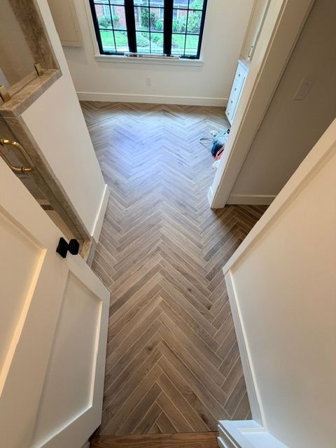 Hallway with herringbone wood floor leading to a windowed room, viewed through open doors.
