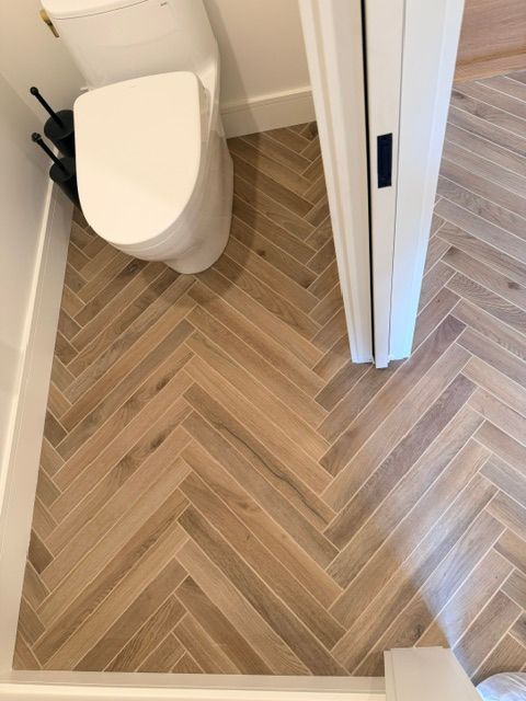 Small bathroom with a toilet and herringbone wood-look tile floor.