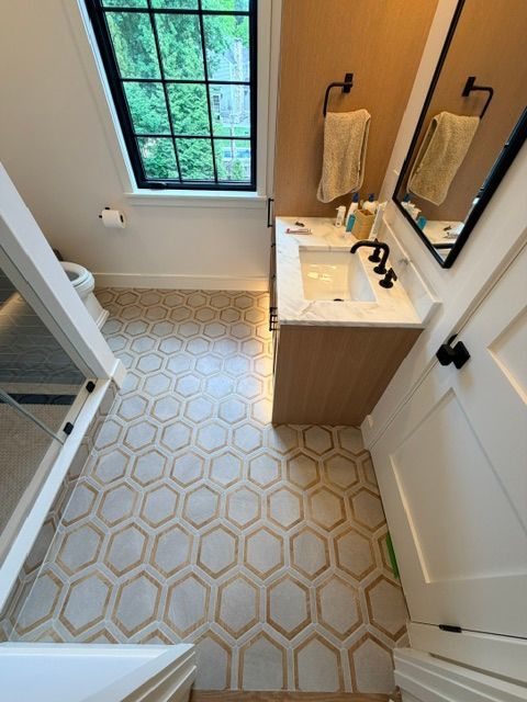 Small bathroom with patterned tile floor, vanity sink, toilet, window, and shower curtain.