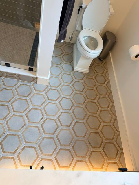 Small bathroom with hexagon tile floor and a toilet beside a glass shower.