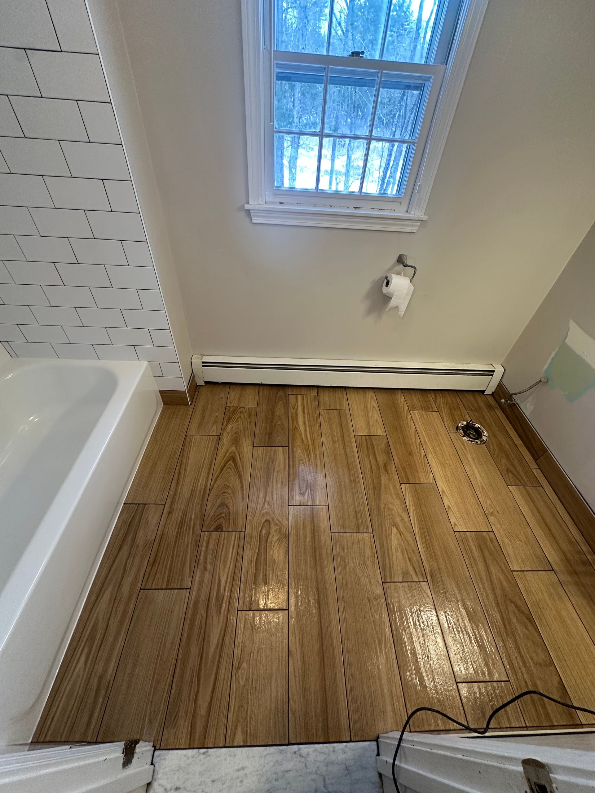 Bathroom with wet wood floor, bathtub edge, and window above a small wall light.