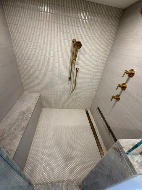 Modern tiled shower with built-in bench, handheld shower, and wall-mounted fixtures.