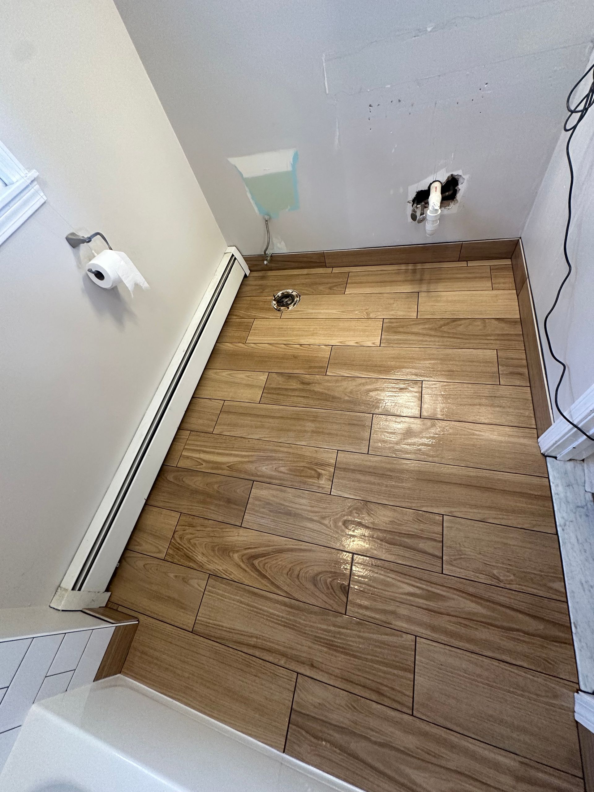 Damaged wood floor in a small room, with cutouts in the wall and exposed plumbing fixtures.