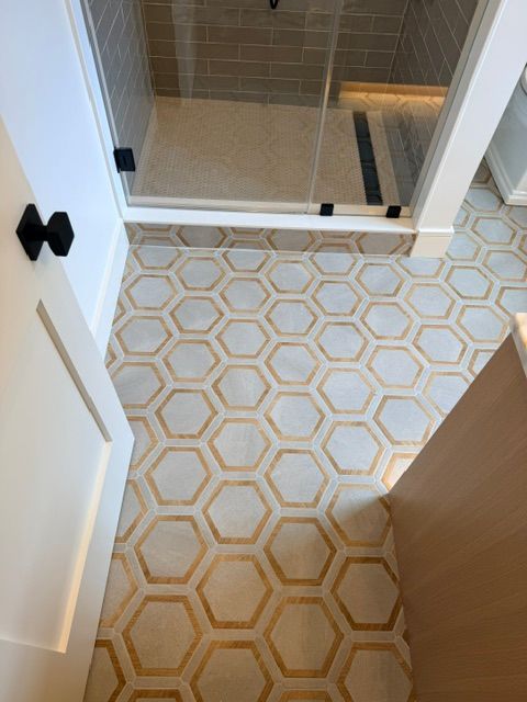 Patterned bathroom floor tiles leading to a glass shower door and beige tiled shower stall.