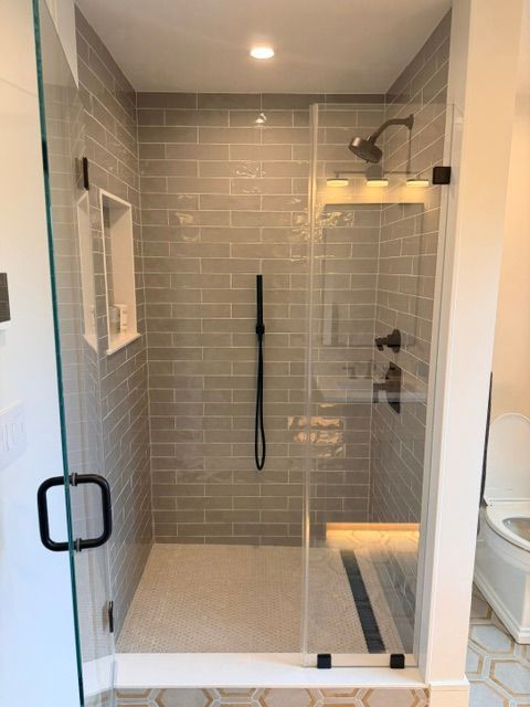 Small tiled walk-in shower with glass door, black fixtures, and a handheld showerhead.
