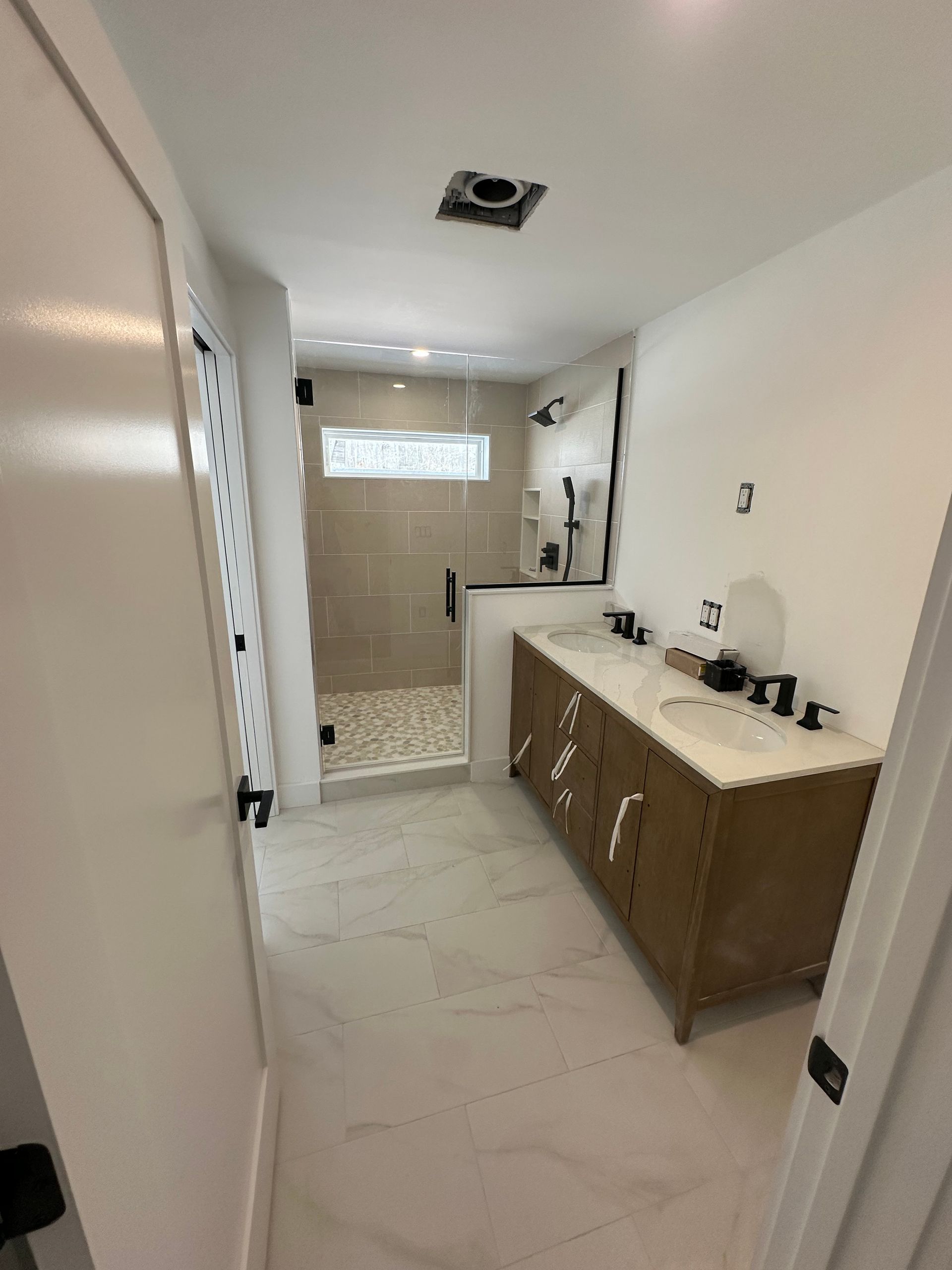 Narrow white bathroom with vanity, shower at the back, and a ceiling vent opening exposed above.