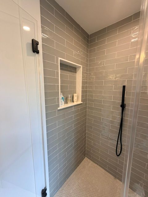 Modern tiled shower with a built-in niche, black showerhead, and glass door.