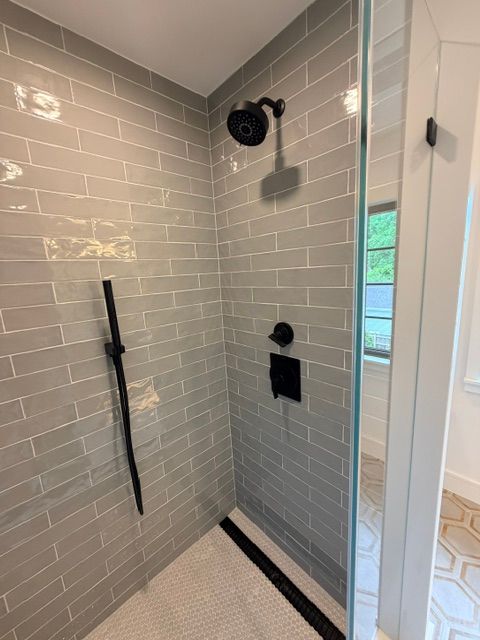 Tiled walk-in shower with black fixtures, glass door, and a low black drain channel.