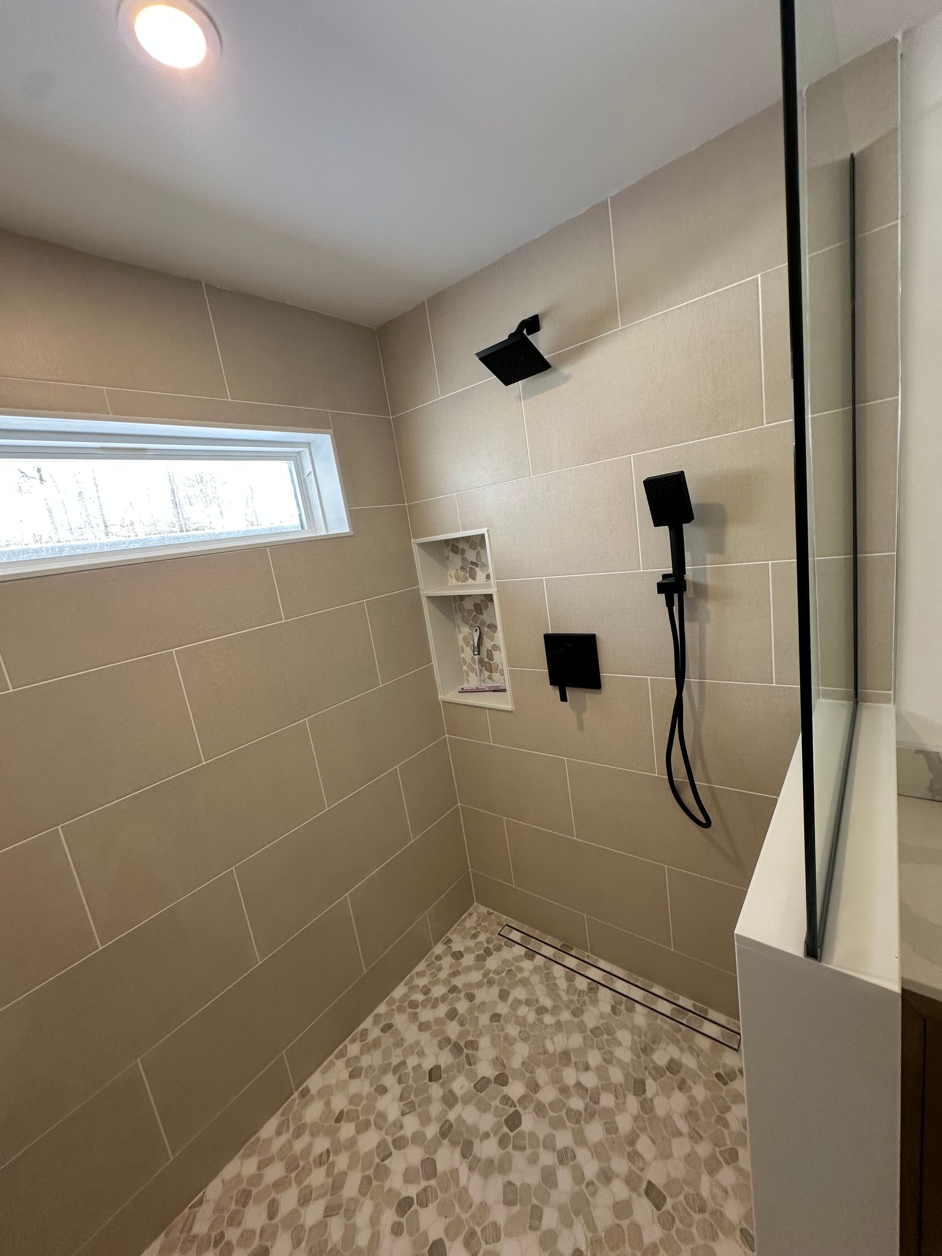 Small tiled bathroom shower with a narrow window, built-in shelf, and wall-mounted fixtures.