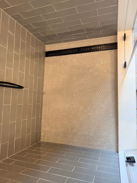 Tiled shower stall with a built-in bench and dark shelf ledge near the ceiling.