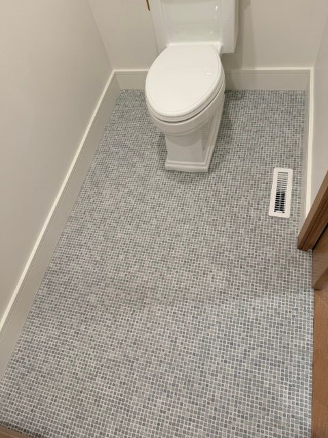 Small bathroom with a toilet, gray patterned carpet, and a floor vent.