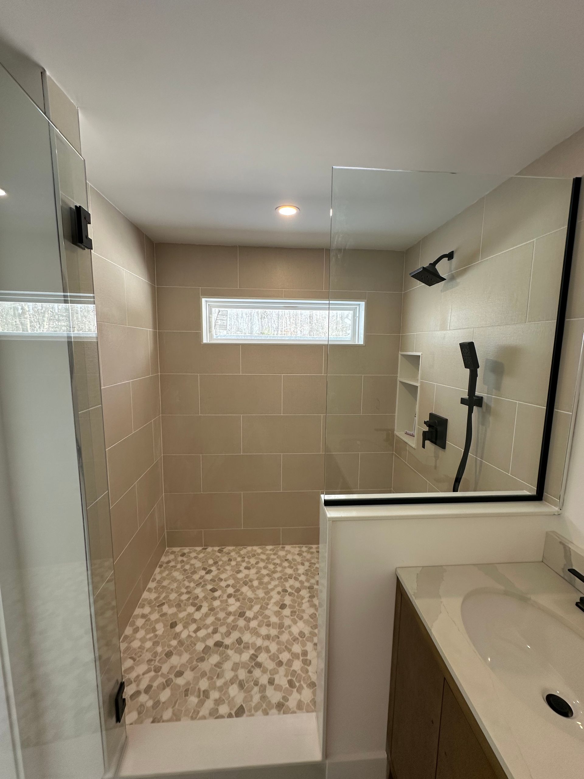 Modern bathroom with walk-in tiled shower, glass partition, and sink vanity.