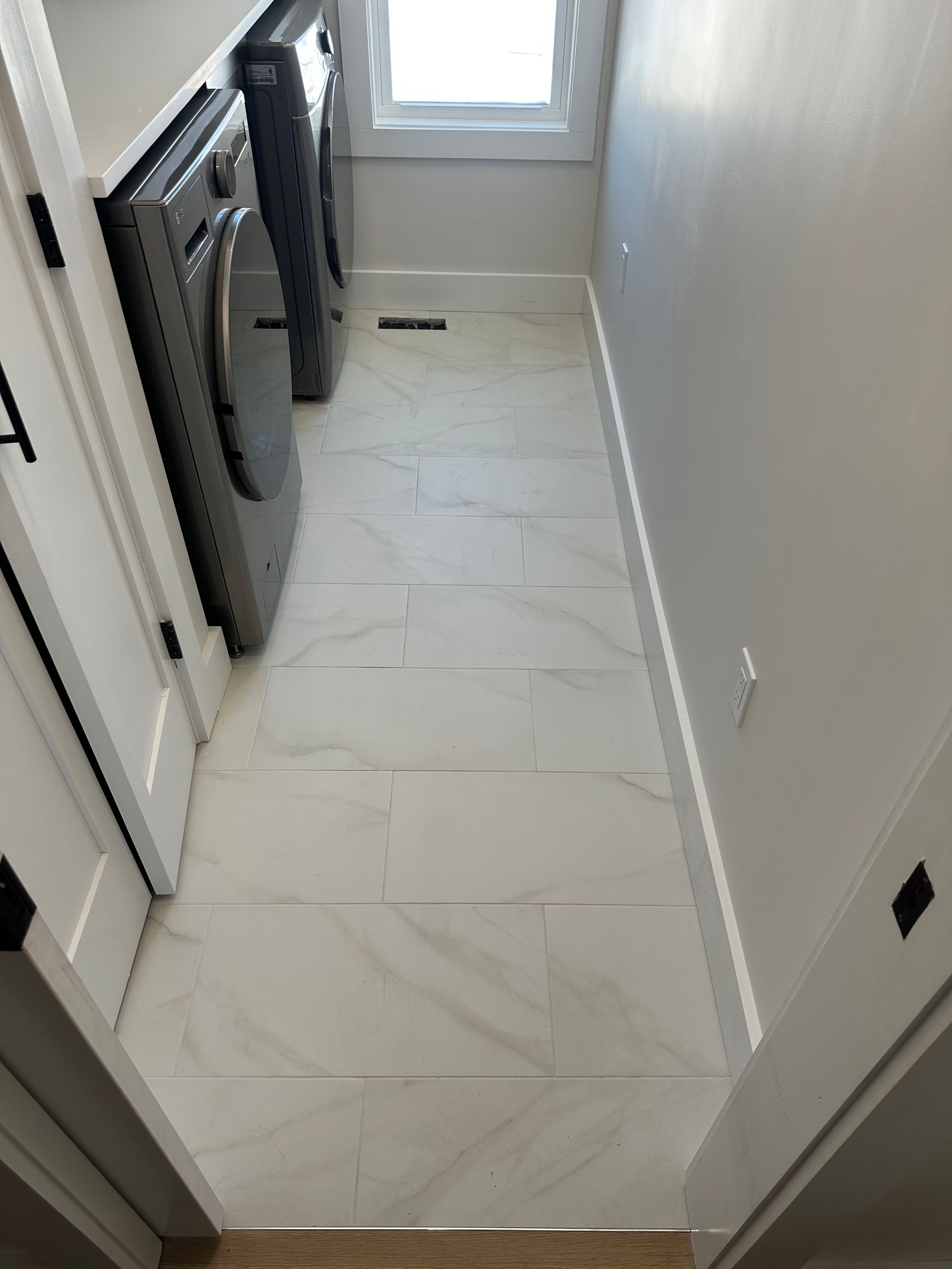 Narrow hallway with white marble tile flooring, gray walls, and a window at the end.