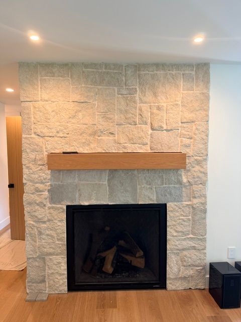 Stone fireplace with a black firebox and wooden mantel in a light-colored room.
