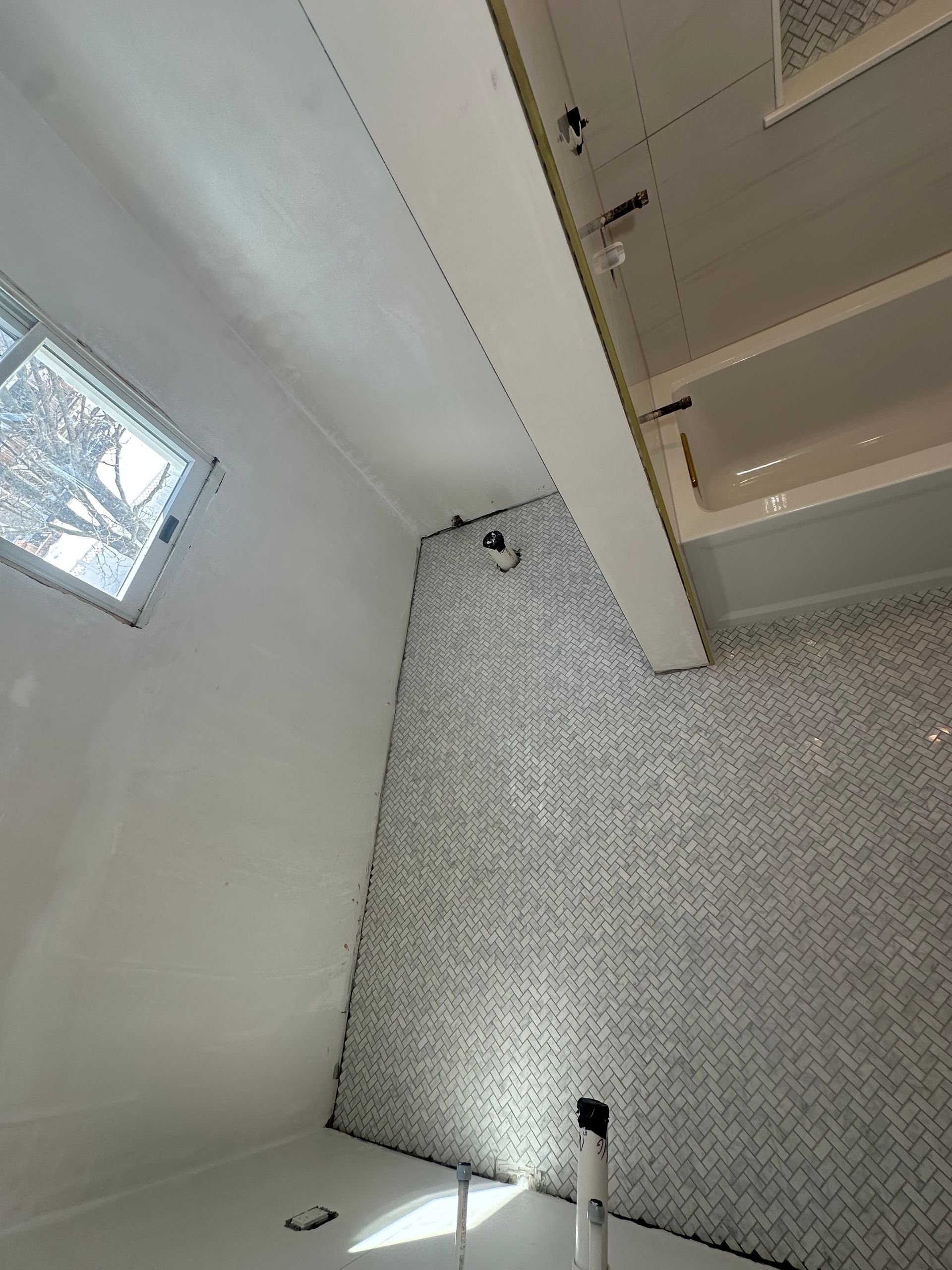 Tilted view of a bathroom with white walls, mosaic tile floor, a window, and a shower area.