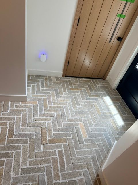 Hallway with herringbone tile floor, wooden closet doors, and a small glowing device on the wall.