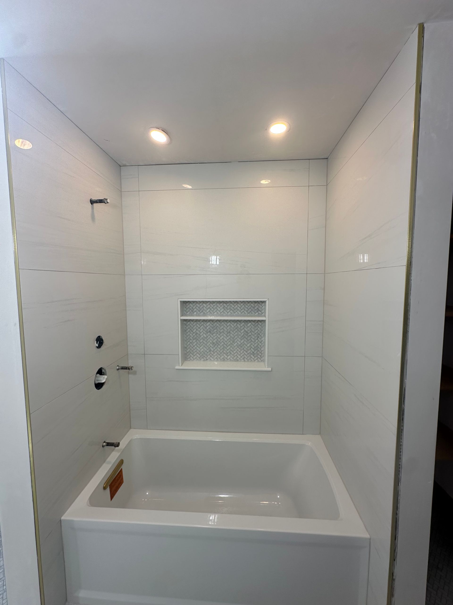Empty white bathroom with a bathtub, tiled walls, recessed lights, and a built-in wall niche.