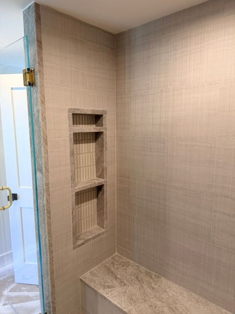 Built-in tiled shower niche above a marble bench in a beige bathroom.