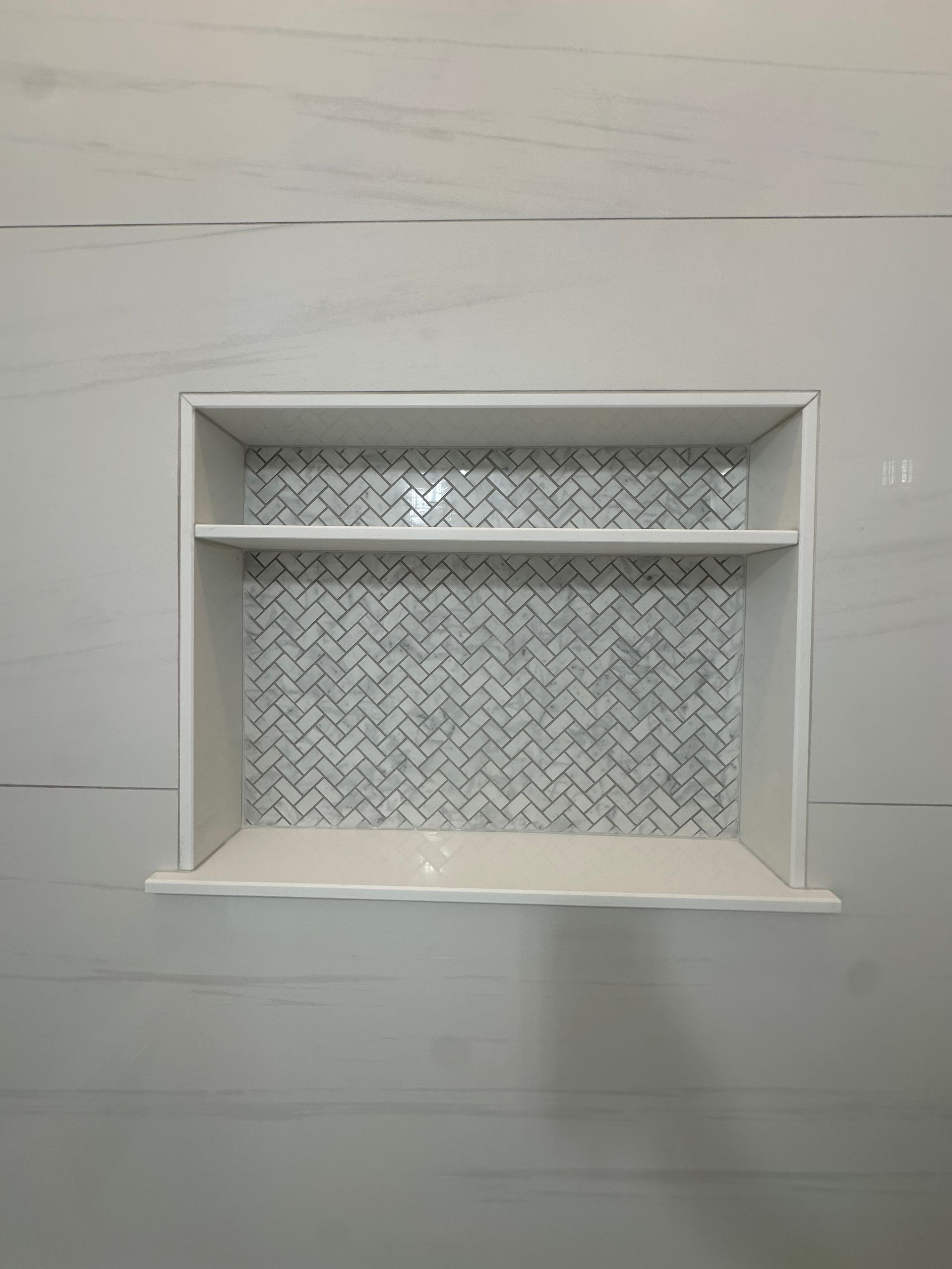 Built-in wall niche with white shelves and a patterned back panel