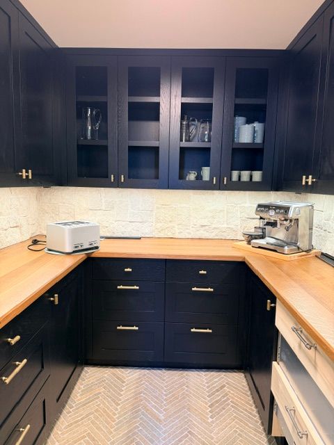 Black kitchen with dark cabinets, wooden counters, and a herringbone runner rug.