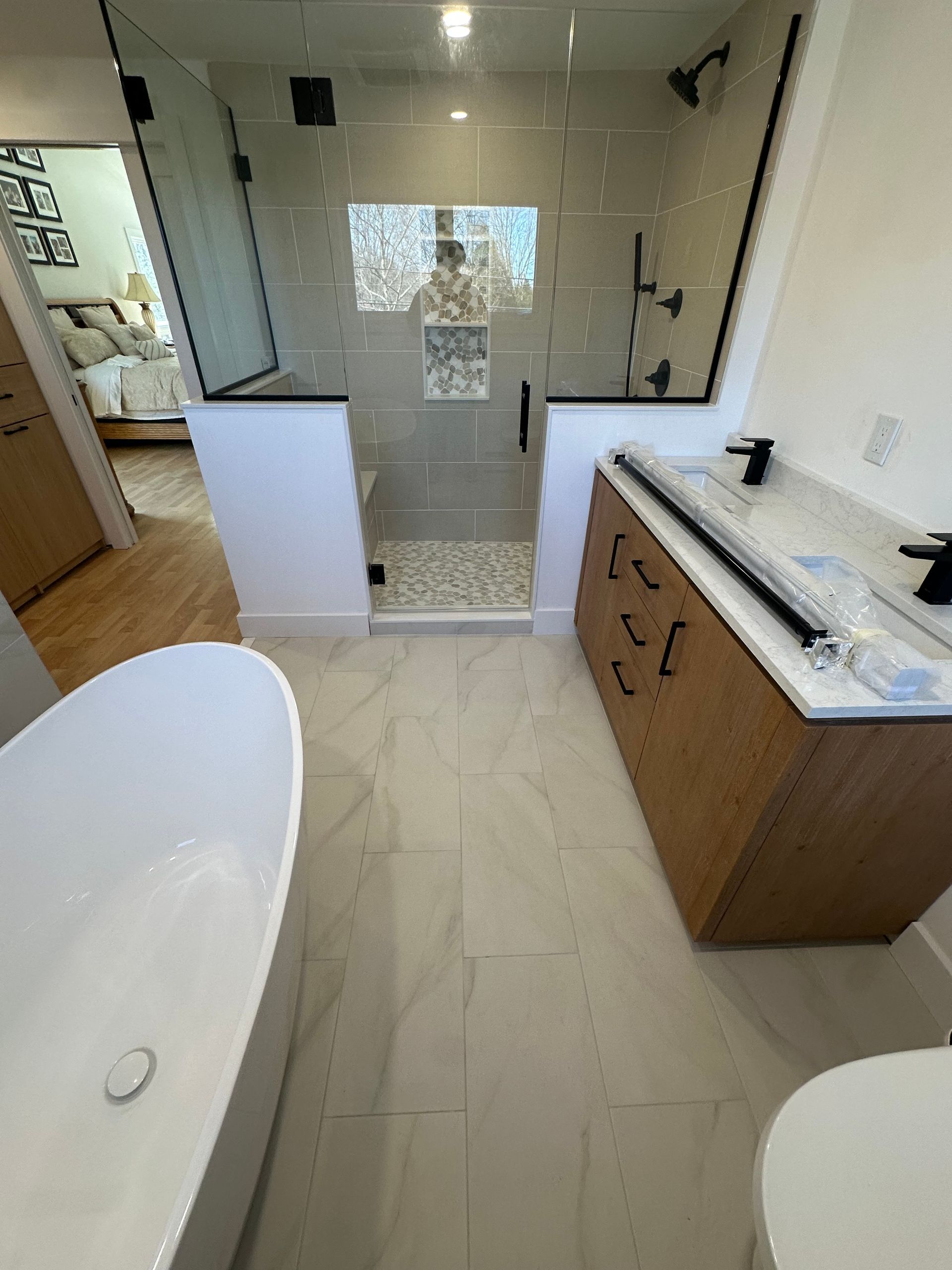 Modern bathroom with freestanding tub, glass shower, white tile, and wood vanity with marble countertop